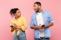 Black man with cellphone spying on his girlfriend chatting on mobile phone, posing on pink studio background Royalty Free Stock Photo