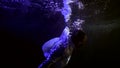 Black man is diving underwater in dark deep pool, subaquatic shot of sinking persone