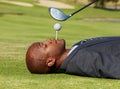 Black man, face and lying on golf course with tee in mouth for hole in one on green grass or field. African male person Royalty Free Stock Photo