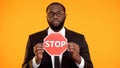 Black man in formal suit showing stop sign, antiracism campaign, social equality