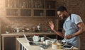 Black man baking pastry and using laptop in kitchen Royalty Free Stock Photo