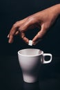 Black man hand hold cube of sugar above white cup