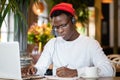 Black man in headphones wear red hat, watching educational webinar on laptop, remotely online work in cafe, listening audio lesson Royalty Free Stock Photo