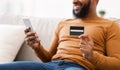 Black Man Holding Credit Card Using Phone Sitting At Home Royalty Free Stock Photo