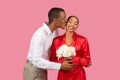 Black man kissing woman's cheek, she holds flowers, love and affection display