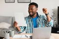 Black Man At Laptop Celebrating Success Holding Paper At Workplace Royalty Free Stock Photo