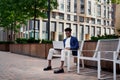 Black man with laptop works on street near city business center. Fashionable businessman outdoors