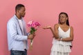 Black man making surprise for bored woman giving flowers