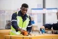 Black man professional worker wearing safety uniform and hard hat using packing tape on packaging cardboard box product in Royalty Free Stock Photo