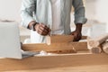 Blog about repair furniture and carpentry. Black man screwing bolt to wooden table leg and using laptop at home interior