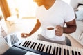 A black man sits in the living room of his apartment and plays a synthesizer. He composes music and drinks coffee. Royalty Free Stock Photo