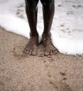 Black man sitting on the beach with waves hitting his legs. Bare feet in the sand