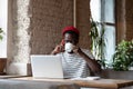 Black man talking on mobile phone, drinking coffee, remotely online work on laptop in cafe Royalty Free Stock Photo