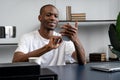 Black man uses a smartphone while sitting at a desk in the office. A happy young man communicating with colleagues and Royalty Free Stock Photo