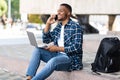 Black man using laptop, sitting in the city with phone Royalty Free Stock Photo