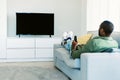 Black man watching TV with blank screen, holding remote control and switching channels on flatscreen plasma, mockup