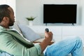 Black man watching tv, looking at black blank television monitor for mock up template, man using remote controller