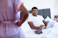 Black man and woman in the bedroom. A man is lying on the bed with laptop. Before him is his girl in lingerie.