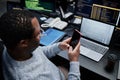 Young Adult Black Man Using Smartphone While Working on Laptop in Office Royalty Free Stock Photo