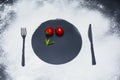 On a black marble background flour powder powdered snow silhouette plate plate fork knife appliances in the center tomato and mint