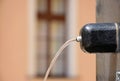 Black marble fountain spout with flowing water stream. blurred facade background.