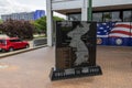 A black marble Korean War Memorial at Louisiana Memorial Plaza with cars on the street and lush green trees and grass