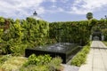 A black marble water fountain surrounded by lush green trees and plants and colorful flowers with blue sky and clouds