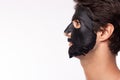 Black mask on face with well groomed man getting spa treatments. Handsome young man putting Moisturizer rejuvenating black mask on