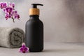 A black matte bottle and rolled grey towel and a vibrant purple orchid flower accentuate the spa-like atmosphere