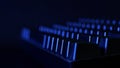 Black mechanical gaming computer keyboard illuminated in the dark by blue light from a monitor screen. Side view. Copy space.