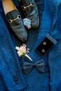 Black men shoes stand on a blue suit next to a watch and boutonniere