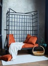 Black metal armchair in the loft style interior. Orange soft pillows and a white linen bedspread Royalty Free Stock Photo