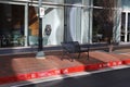 A black metal bench on a red brick sidewalk in front of the glass window of some shops with a red painted curb Royalty Free Stock Photo