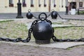 Black metal chain with large links and round heavy weights lies on concrete slabs on the ground.