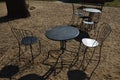 Black metal chairs and round tables in a cafe on a cobbled square with a sand surface of compacted yellow gravel under an old tree Royalty Free Stock Photo