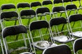 Black metal chairs stand outside in the park in the rain. Empty auditorium, green grass, waterdrops, closeup Royalty Free Stock Photo