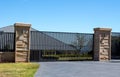 Black metal driveway entrance gates set in sandstone brick fence with residential garden