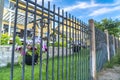 Black metal fence with potted colorful flowers against blurry homes and blue sky