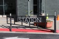 A black metal gate with the word `Station` on the front surrounded by street cones a red curb and black building