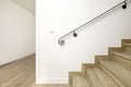 Black metal handrail attached to a white wall on a staircase with wooden steps of a two-story single-family residential home Royalty Free Stock Photo