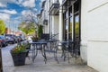 Black metal tables and chairs in an outside dinning area at a restaurant in front of a white building with lush green trees