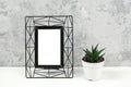 Black metal vertical frame with white blank and succulent flower on table against grey concrete wall. Mockup Template for your Royalty Free Stock Photo