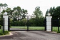 Black metal wrought iron driveway property entrance gates  set in brick fence, lights, green grass, garden trees Royalty Free Stock Photo