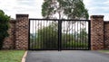 Black metal wrought iron driveway property entrance gates set in brick fence, lights, green grass, garden trees