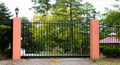 Black metal wrought iron driveway property entrance gates set in brick fence, lights, green grass, garden trees