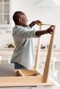 Black millennial handyman assembling wooden table and measuring the width between legs, standing in kitchen, crop