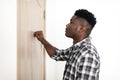 Black Millennial Man Knocking At Closed Door Of Apartment Indoors