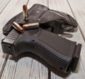 A holstered black pistol with several bullets on a wooden table