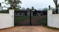 Black modern metal driveway property entrance gates set in concrete fence, lights, trees