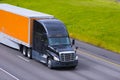 Black modern semi truck orange trailer driving highway line Royalty Free Stock Photo